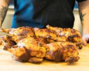a tattooed man standing with many whole chickens on a cutting board