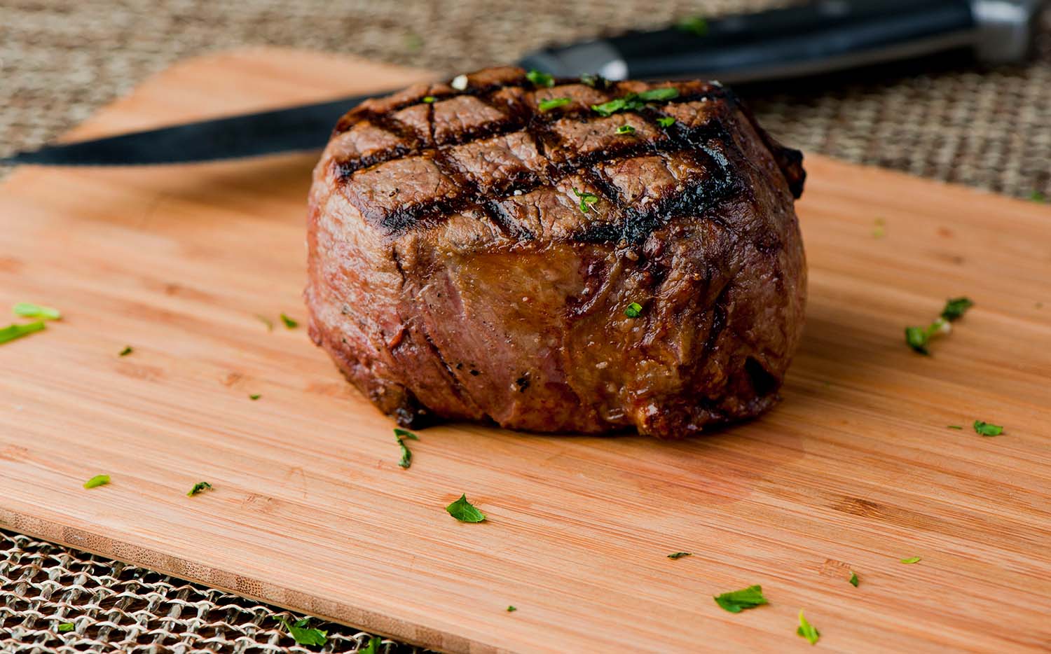 grass-fed-beef-meat-protein cut of filet mignon sitting on a cutting board with herbs sprinkled around it
